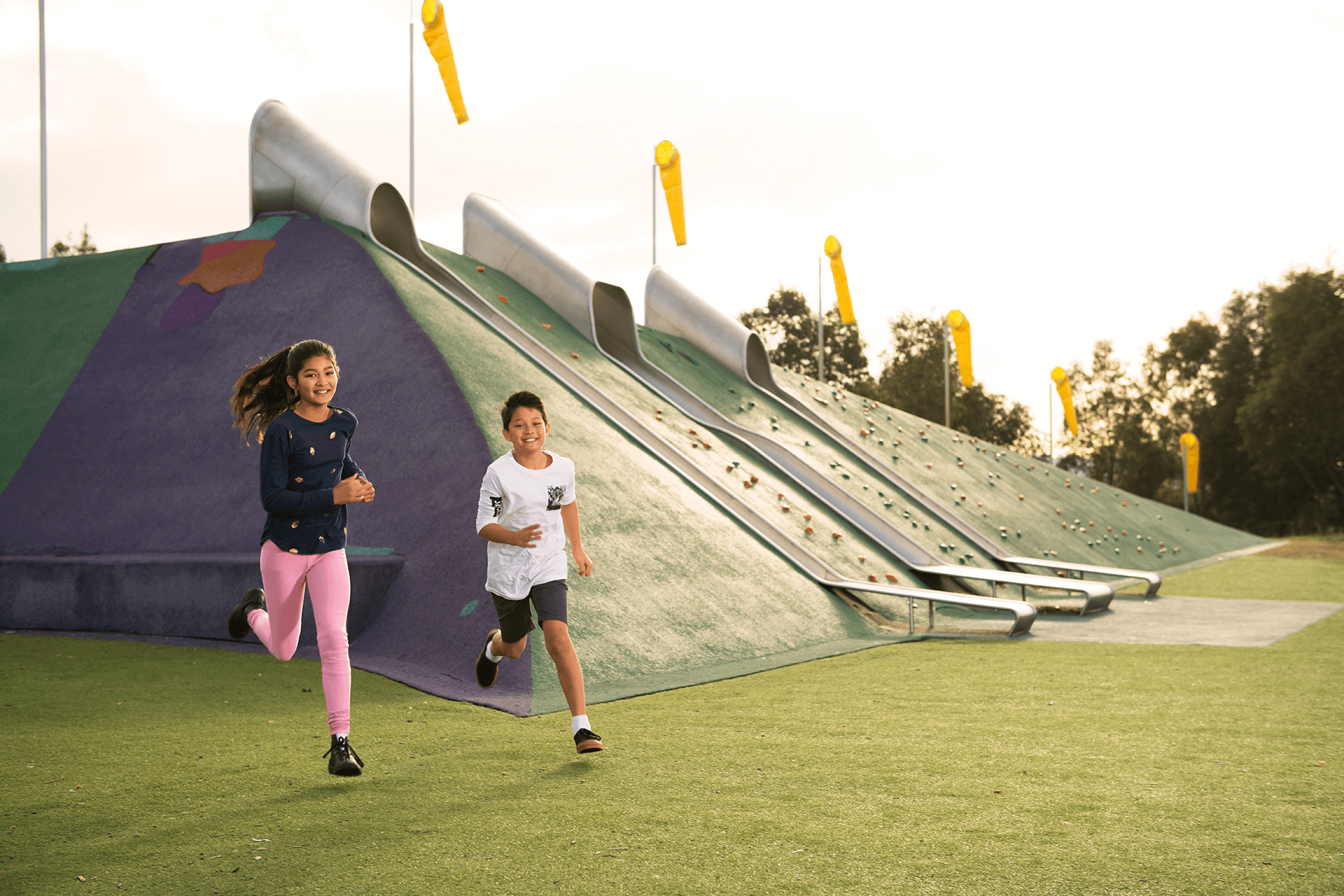 Two young people running in front of climbing wall and slippery slides.